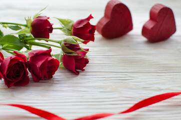 Red roses decorated with red ribbon and two wooden hearts on white wooden background