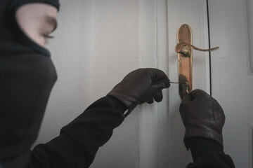 Burglar holding Lock-picker to open a housedoor. Home Burglar in a Mask Breaking Into the House....