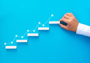Businessman hand arranging wood block stacking as step stair with growing arrow  graph. Business...