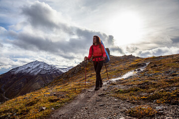 Woman Backpacking along Scenic Hiking Trail surrounded by Mountains in Canadian Nature. Season change from Fall to Winter. Taken in Tombstone Territorial Park, Yukon, Canada.