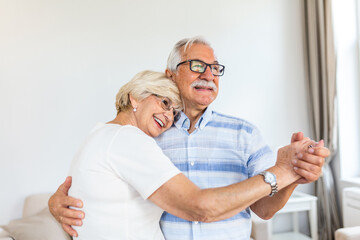 Happy mature loving couple dancing in living room relaxing at home on weekend together, smiling...