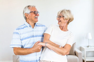Obraz premium Joyful active old retired romantic couple dancing laughing in living room, happy middle aged wife and elder husband having fun at home, smiling senior family grandparents relaxing bonding together