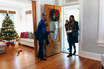 Senior Black woman greeting family at the door for Christmas