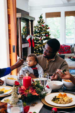 Family eating holiday meal together at dining room table with Christmas tree in background