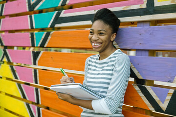Young Black female teenager drawing in notebook at school