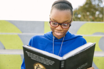 Black female teenager with glasses studying for school outside