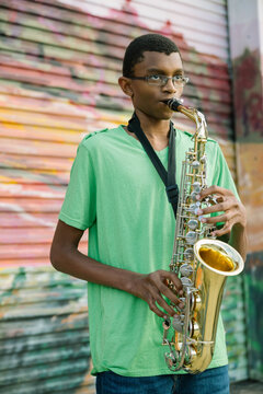 Black teen male playing saxophone at school on colorful background