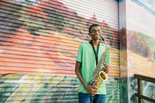 Portrait of Black male teenager playing saxophone at school on colorful background