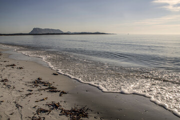 Sunrise on white sand beach. Sea view and mountain on horizon in Sardinia. 