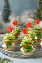 Festive canapes in the shape of Christmas trees made of cucumbers and stars bell pepper on light blue background, Closeup. Vertical format