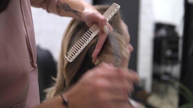 Art of hairdressing. Blonde woman getting her hair hair cut with scissors and hair comb