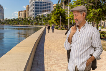 Casually dressed, a mature man takes a walk alongside the waterfront downtown. He looks at the...