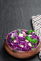 Vegetarian salad with red cabbage and apple in wooden bowl on black stone background