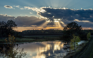 Sun ray behind autumn clods reflect in the waters of a pond