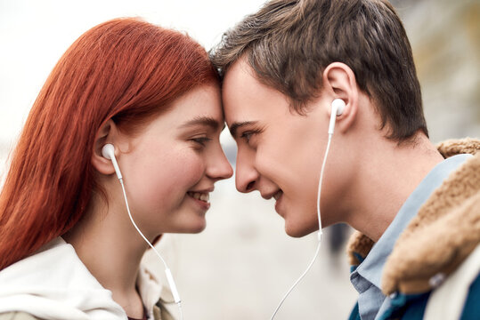 Close Up Of Happy Couple Of Teenagers Listening To Music Using The Same Pair Of Earphones, Looking At Each Other With Love