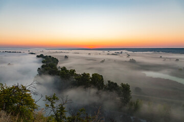 Beautiful panoramic landscape with river valley covered by thick fog in autumn in the early morning. Sunrise.