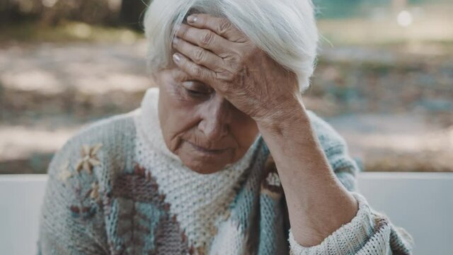 Old worried gray haired woman sitting on the bench and praying. High quality 4k footage