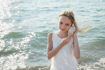 Portrait of beautiful little girl is playing with seashell in sea waves.