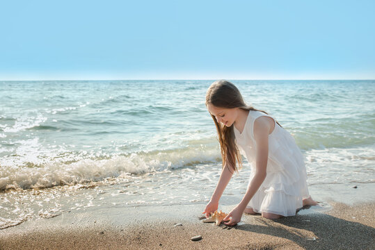 Portrait of beautiful little girl is playing with seashell in sea waves.