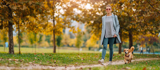 Happy woman walking on a park trail with a dog in autumn
