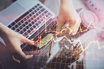 Double exposure of businesswoman hands typing on computer and financial graph hologram drawing. Stock market analysis concept.