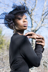 Portrait of young African American woman standing in winter forest. Side on view. Black shirt and...