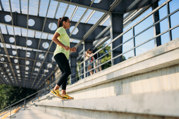 Positive slim woman running up on stairs at city stadium