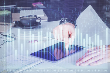 Double exposure of man's hands holding and using a digital device and forex graph drawing. Financial market concept.
