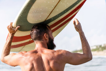 Young hipster man with surfboard on his head greeting friends with a gesture - Guy having fun doing...