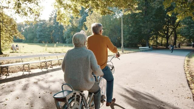 Senior couple riding double bicycle in autumn. Grandmother and grandfather cycling together . Elderly people healthy and active lifestyle. High quality 4k footage