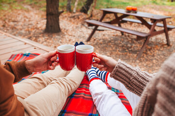 Hot cups of tea in hands in woollen sweater on background of cozy house