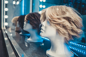 White foam female mannequins heads in a row on a store window at night. Blue and white neon lights...