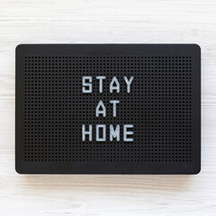 'Stay at home' words on a black lightbox on a white wooden surface, view from above. Top view, overhead, flat lay.