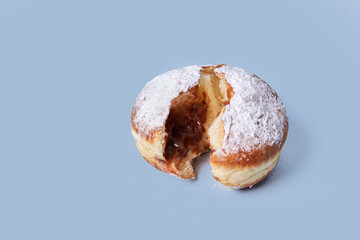 One sweet doughnut is broken in the middle, the filling is visible inside. Isolated on a blue background. High-calorie food.