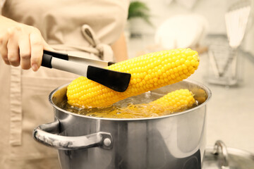 Woman taking boiled corn from pot with tongs in kitchen, closeup