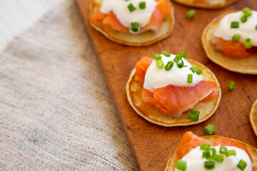 Homemade Blini with Smoked Salmon, Creme and Chives on a rustic wooden board, side view. Space for text.