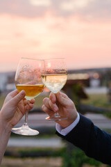 Close up of glasses of wine in the hands of a man and a woman sunset background