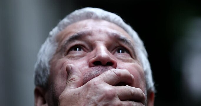 Preoccupied older man looking at sky covering mouth with hand in horror