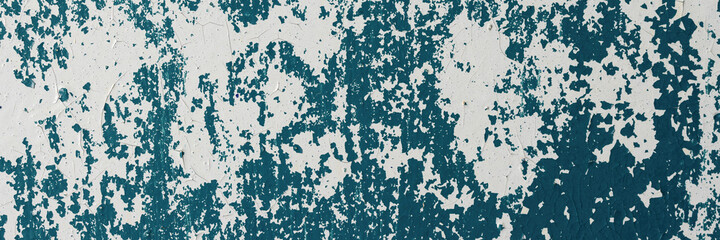 Peeling paint on the wall. Panorama of a concrete wall with old cracked flaking paint. Weathered rough painted surface with patterns of cracks and peeling. Grunge texture for wide panoramic background