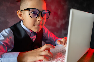 Little businessman child with glasses looks at laptop screen in shock.