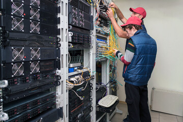 Two technicians switch fiber optic wires at the central router. Installers work in the data center server room. Maintenance of the hosting site.