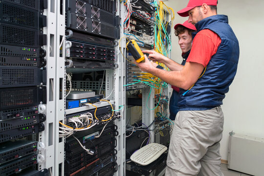 Two people work in a modern data center. Two technicians measure the signal level in the fiber optic cable. Serving a central router in a server room.