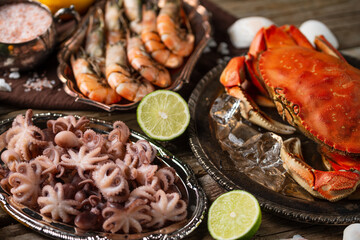 Assorted of seafood on rustic wooden table. Top view of tiger shrimps, cooked crab and baby octopuses served with lime and seashells. Concept of delicious food from the sea or ocean.
