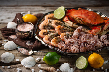 Big round dish with assorted of seafood on wooden table. View of tiger shrimps, cooked crab and baby octopuses served with lime, lemon and seashells. Concept of delicious food from the sea or ocean.