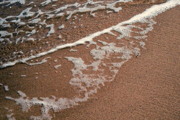 Slightly foamed sea water, pouring out beach sand.