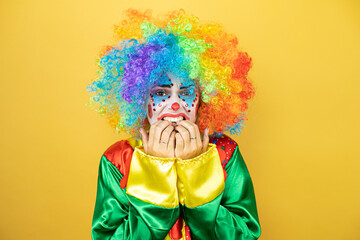 Clown standing over insolated yellow background very nervous.