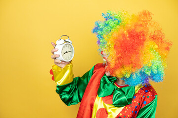 Clown standing over yellow insolated yellow background surprised holding a clock