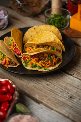 Professional chef in black uniform pours chopped tomatoes on corn tortilla for cooking tacos on dark blue background. Traditional mexican cuisine. Concept of tasty street food. Frozen motion.