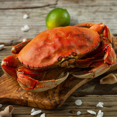 Tasty cooked crab on wooden chopped board served with lime and seashells on rustic wooden table background. Delicious meal. Concept of seafood. Gifts from the sea. Traditional Thai dish.