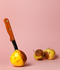 A spoiled Apple with a dark spot with a knife stuck in it, and two rotten fruit in the background.Vertically, with space